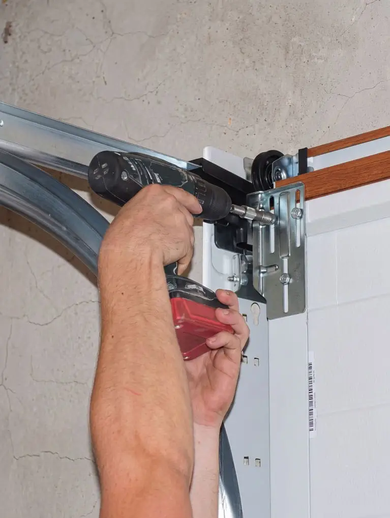 Mr. Goldie Garage Door - Mr. Goldie Garage Door - Person using a drill to install or tighten hardware on a garage door mechanism and track area.
